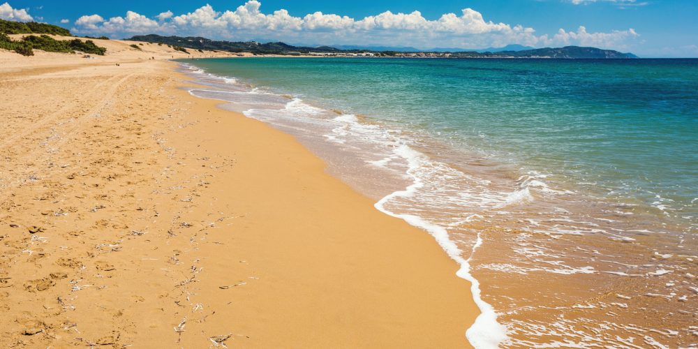 Issos Beach on Corfu Island features a vast expanse of golden sand and clear blue waters, perfect for a day of sun and relaxation